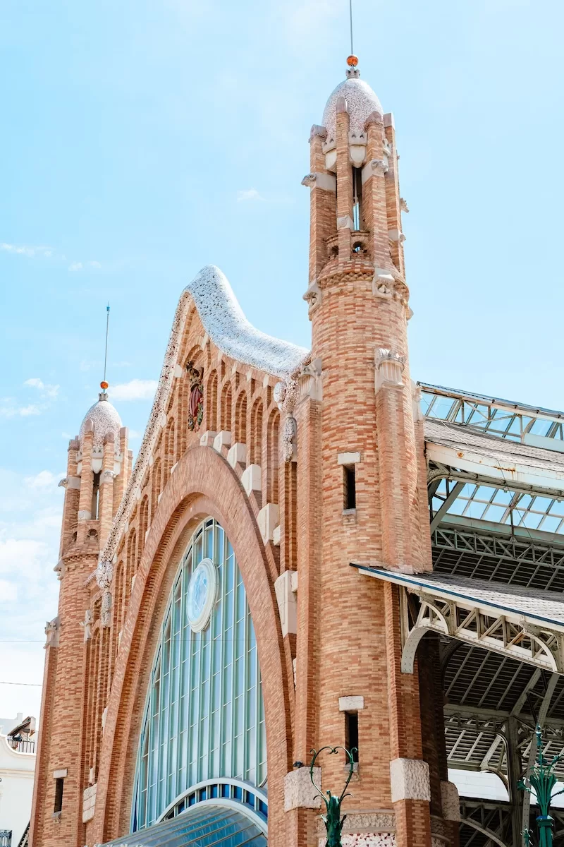 Architectural detail of Valencia’s Central Market exterior with brick towers, arched entrance, and decorative facade against a clear blue sky