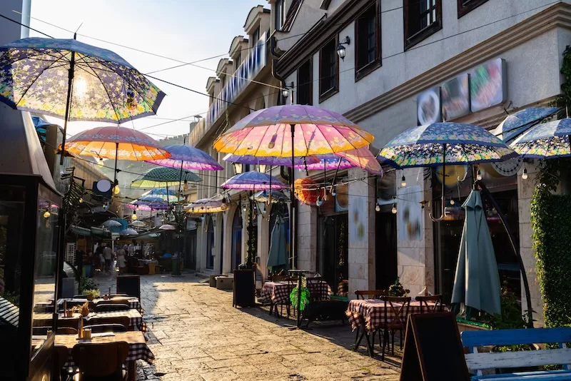 Pedestrian street in North Macedonia lined with cafés and colorful umbrellas hanging overhead.