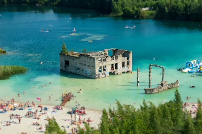 Turquoise lake in Estonia with swimmers, floating attractions, and a partially submerged industrial building.