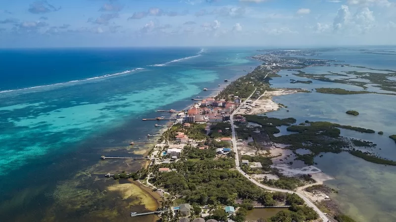 Aerial view of a narrow Caribbean coastline in Belize with turquoise water, island development, mangroves, and a long stretch of low-lying land