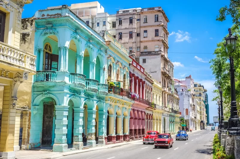 Colorful colonial buildings in Havana with vintage cars driving down a wide street under a clear blue sky
