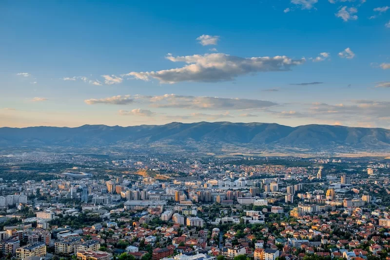 Panoramic view of Skopje with dense city buildings and mountain ranges across the horizon.