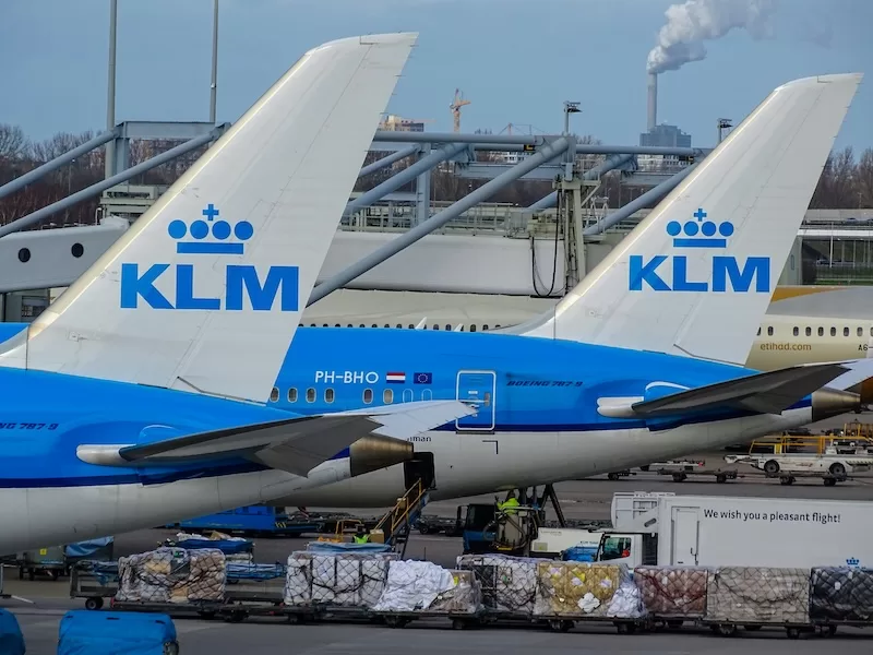KLM aircraft parked on an airport tarmac with cargo and ground operations visible nearby.
