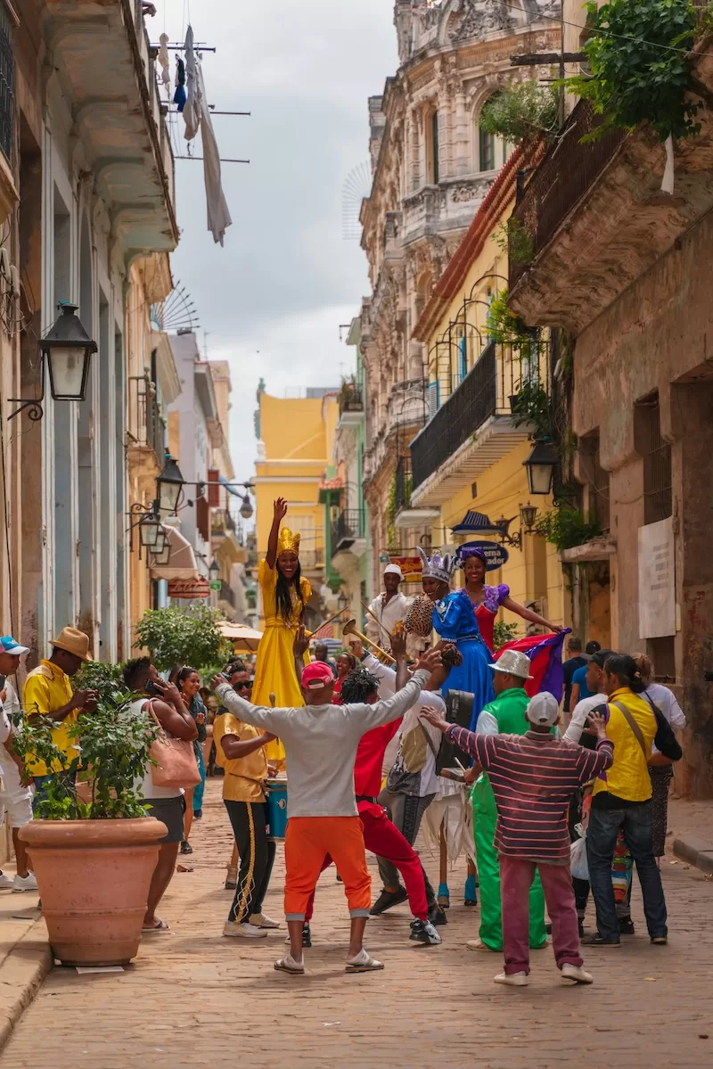 Street celebration in Havana with performers in bright costumes dancing among a gathered crowd on a cobblestone road