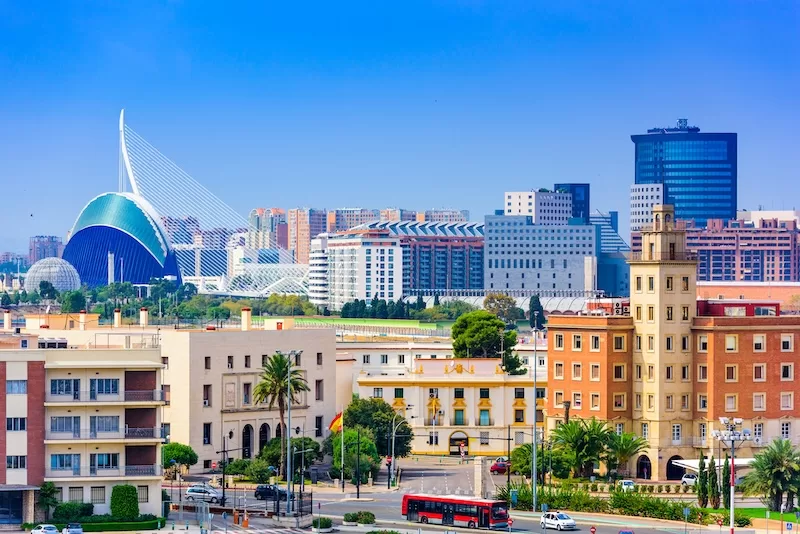 Valencia cityscape with residential buildings, palm trees, and the City of Arts and Sciences visible in the distance under a clear blue sky