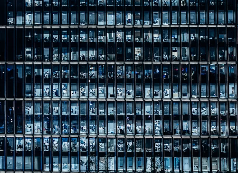 Exterior view of a modern office building at night with many illuminated windows showing financial and corporate activity