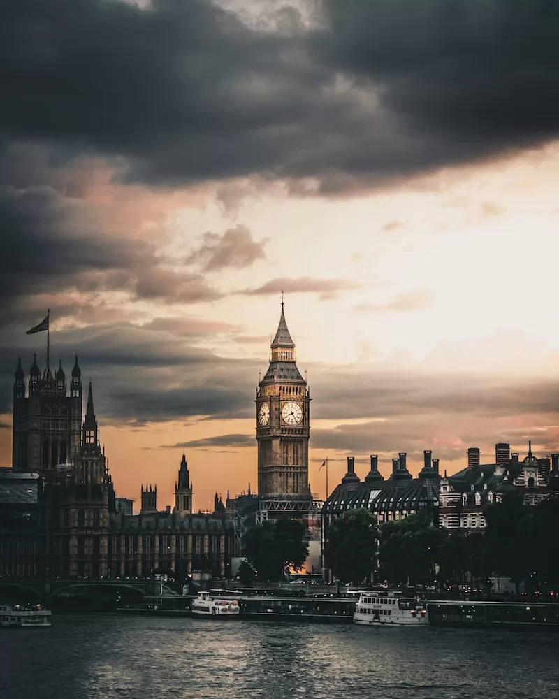 Big Ben and the Palace of Westminster skyline at sunset with dark storm clouds over the River Thames.
