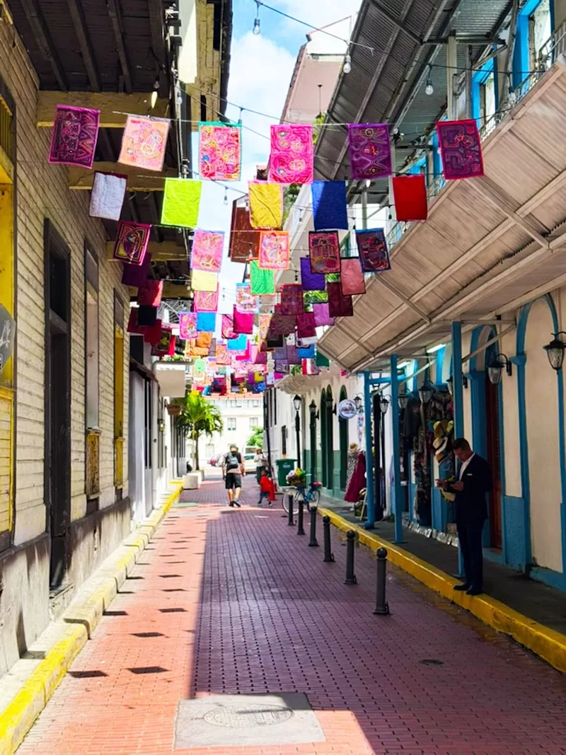 Narrow Panama street decorated with colorful hanging banners above shops and pedestrians below.