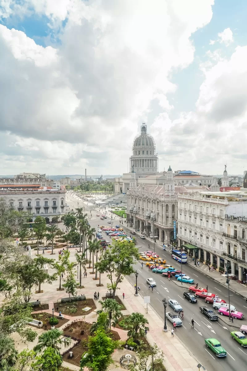 Elevated view of central Havana with historic buildings, colorful classic cars, palm-lined streets, and the Capitol building in the distance