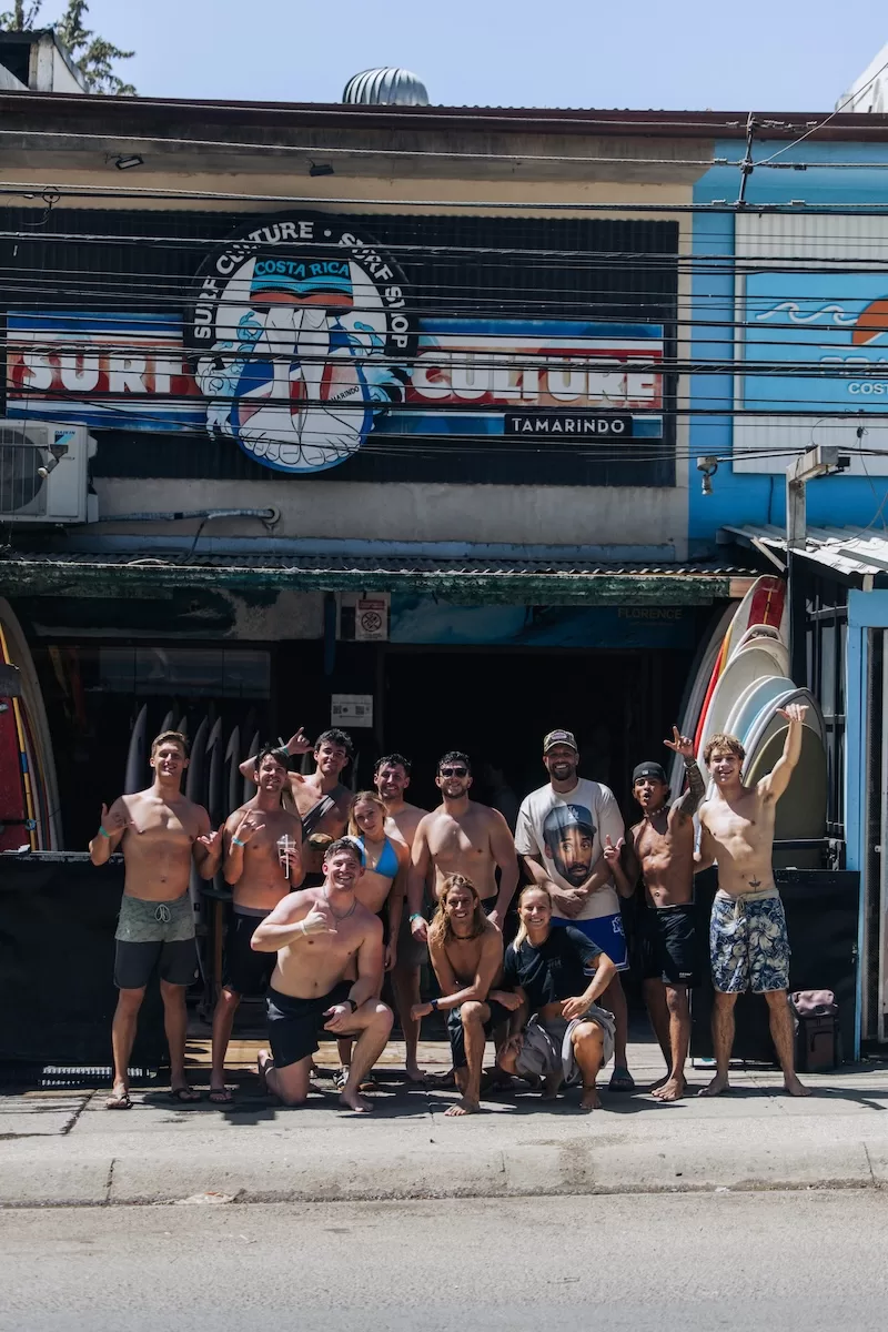Group of young people posing outside a surf shop in Tamarindo, Costa Rica, with surfboards lined up at the entrance