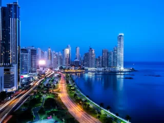 Panama City skyline at night with illuminated towers, coastal boulevard, and light trails running along the waterfront