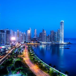 Panama City skyline at night with illuminated towers, coastal boulevard, and light trails running along the waterfront
