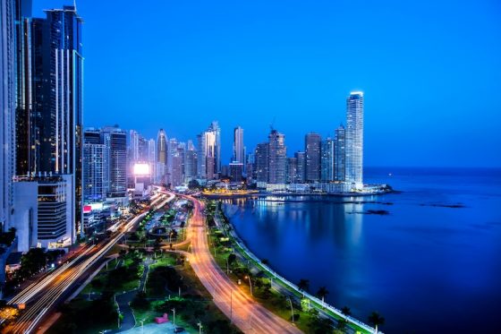 Panama City skyline at night with illuminated towers, coastal boulevard, and light trails running along the waterfront