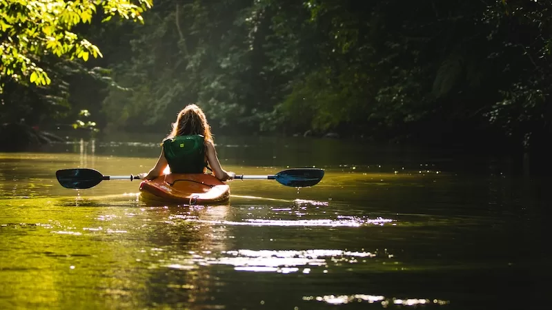 Woman kayaking down a calm river through lush jungle in Costa Rica with sunlight reflecting on the water