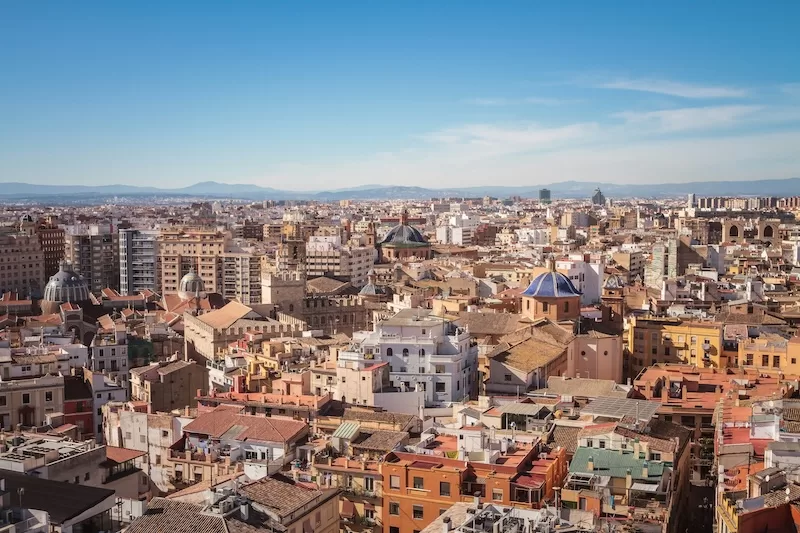 Panoramic view of Valencia rooftops, domes, and city skyline under a clear sky with mountains in the distance