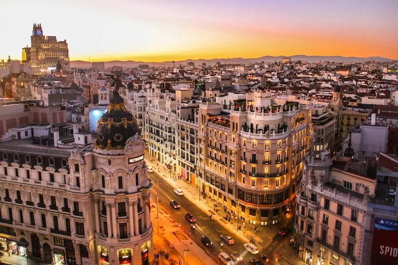 Elevated sunset view over central Madrid with grand historic buildings, glowing streets, and a wide urban skyline