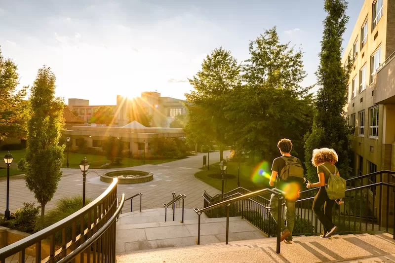 Two students walking across a university campus at sunset, representing international schooling, higher education, and study abroad opportunities.