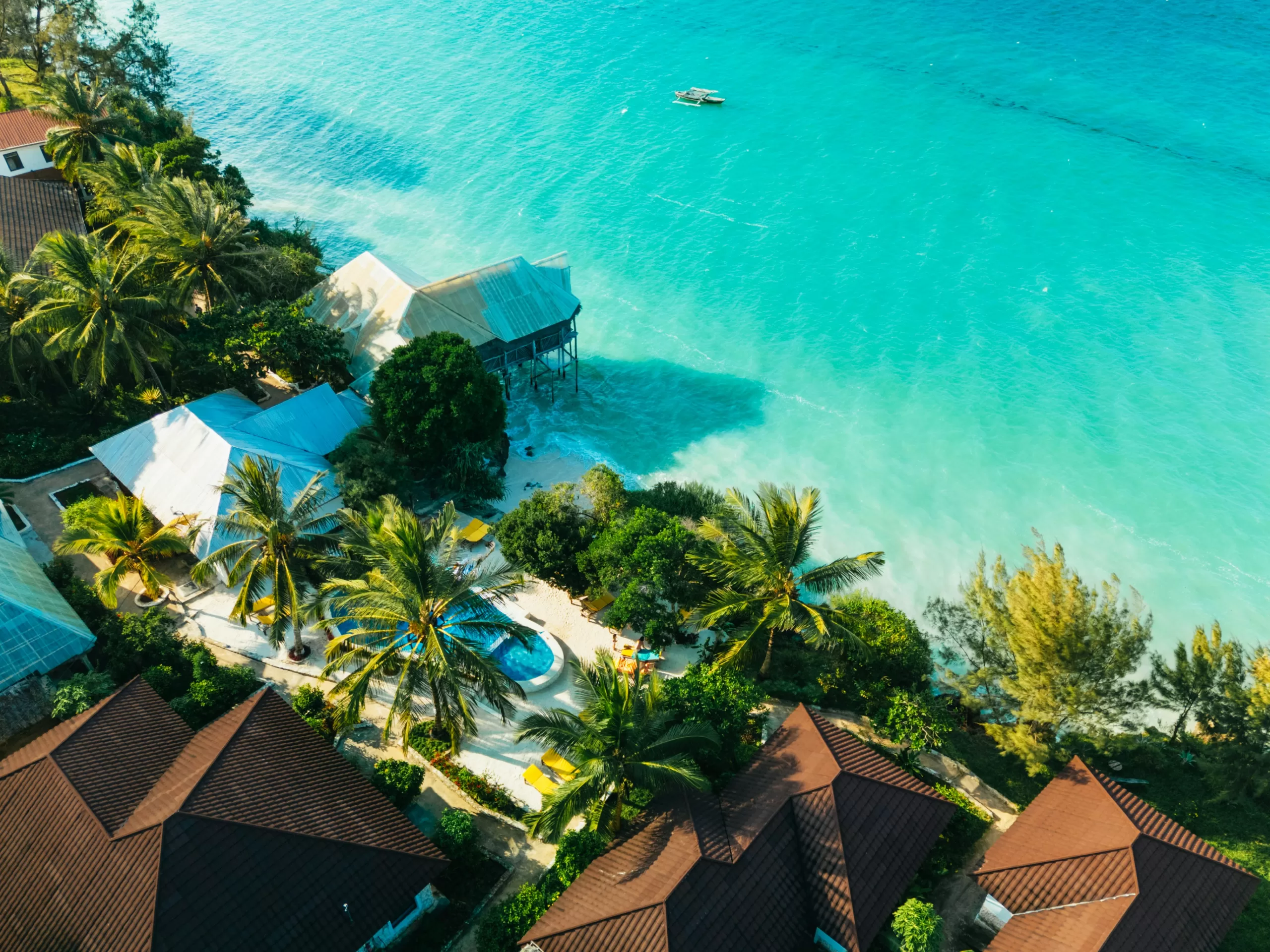 Aerial view of tropical seaside villas, palm trees, and turquoise ocean water along a bright coastal resort shoreline