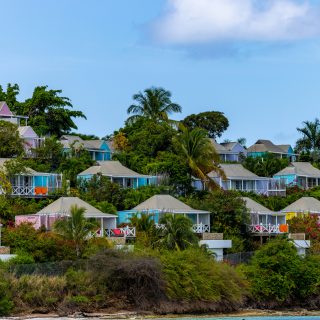 Colorful pastel cottages scattered across a lush hillside with palm trees and tropical greenery overlooking the coast
