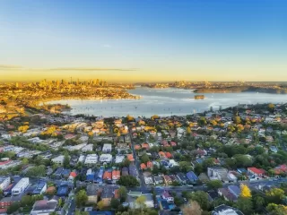 Aerial view of Sydney Harbor and surrounding suburbs at sunset, illustrating Australia’s housing affordability debate