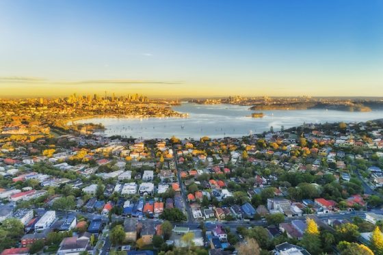 Aerial view of Sydney Harbor and surrounding suburbs at sunset, illustrating Australia’s housing affordability debate