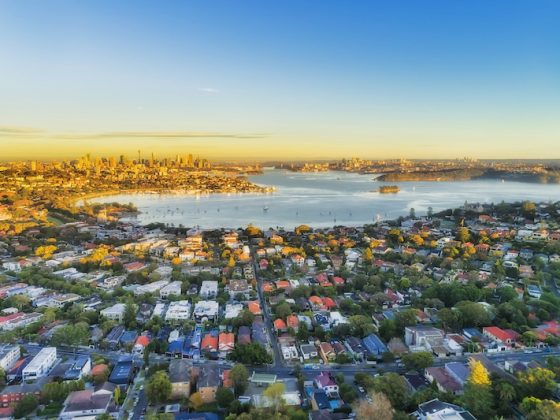 Aerial view of Sydney Harbor and surrounding suburbs at sunset, illustrating Australia’s housing affordability debate