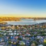 Aerial view of Sydney Harbor and surrounding suburbs at sunset, illustrating Australia’s housing affordability debate