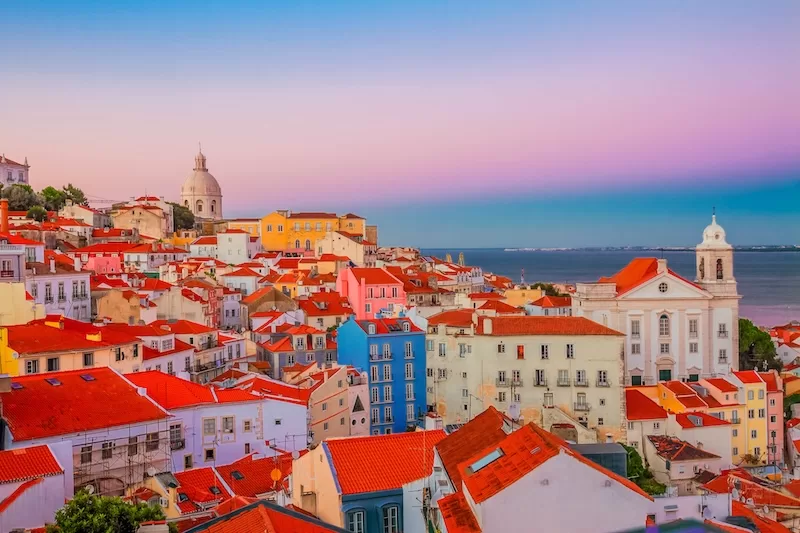 Lisbon rooftops with red tiles overlooking the water at sunset