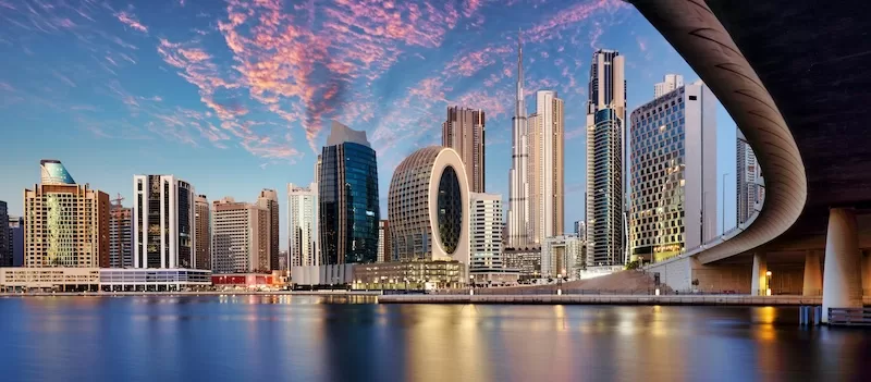 Modern Dubai skyline at sunset with waterfront reflections and high-rise towers