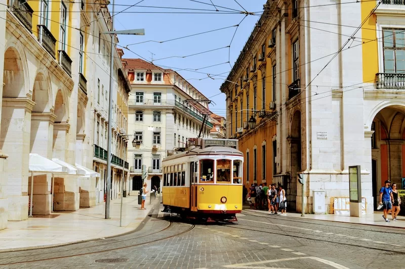 Yellow tram traveling through Lisbon streets, representing European residency and citizenship pathways.