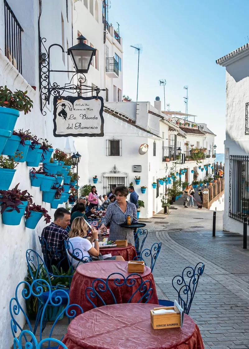 Outdoor café on a whitewashed street in southern Spain with blue flowerpots and diners