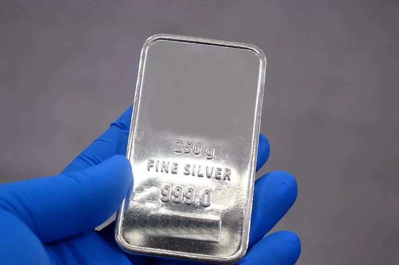 Gloved hand holding a fine silver bar representing physical silver ownership and asset protection