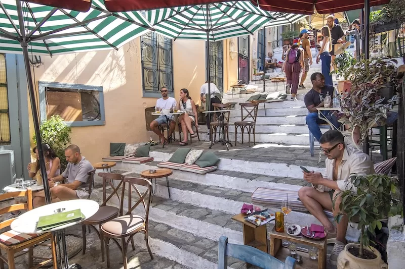 Outdoor café seating on stepped street in Athens with residents and visitors gathered under umbrellas