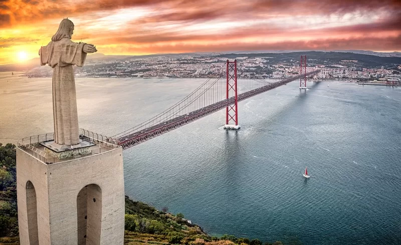 Christ the King statue overlooking Lisbon and the 25 de Abril Bridge at sunset.