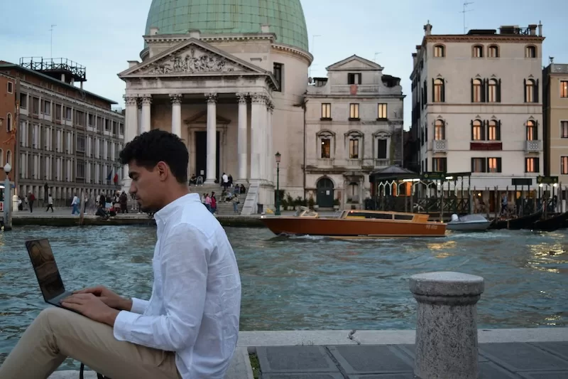 Man working on a laptop beside a canal in Venice, reflecting long-term travel and remote work in Europe