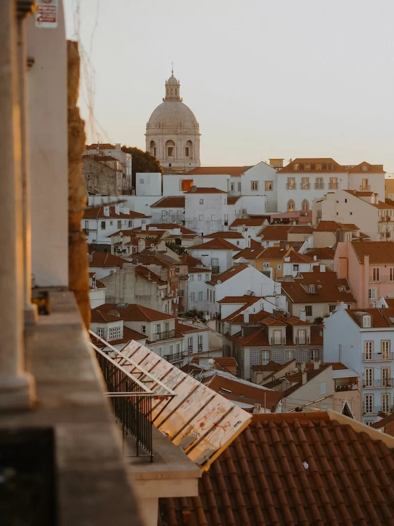Lisbon rooftops and church dome glowing in warm evening light.