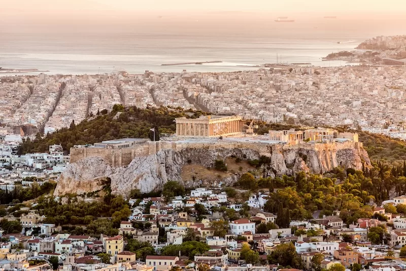 Wide aerial view of the Acropolis rising above Athens with the city spreading to the sea beyond