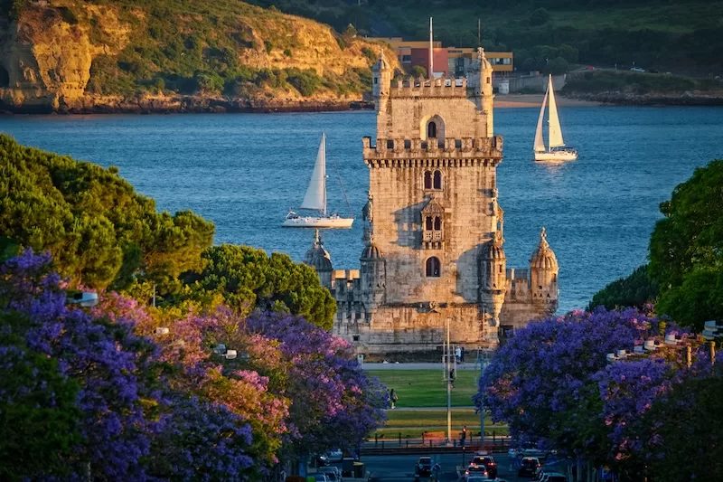 Belém Tower in Lisbon overlooking the Tagus River with sailboats in the background.