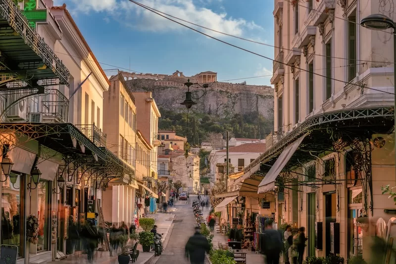 Busy Athens street with shops and the Acropolis visible above the city in the distance