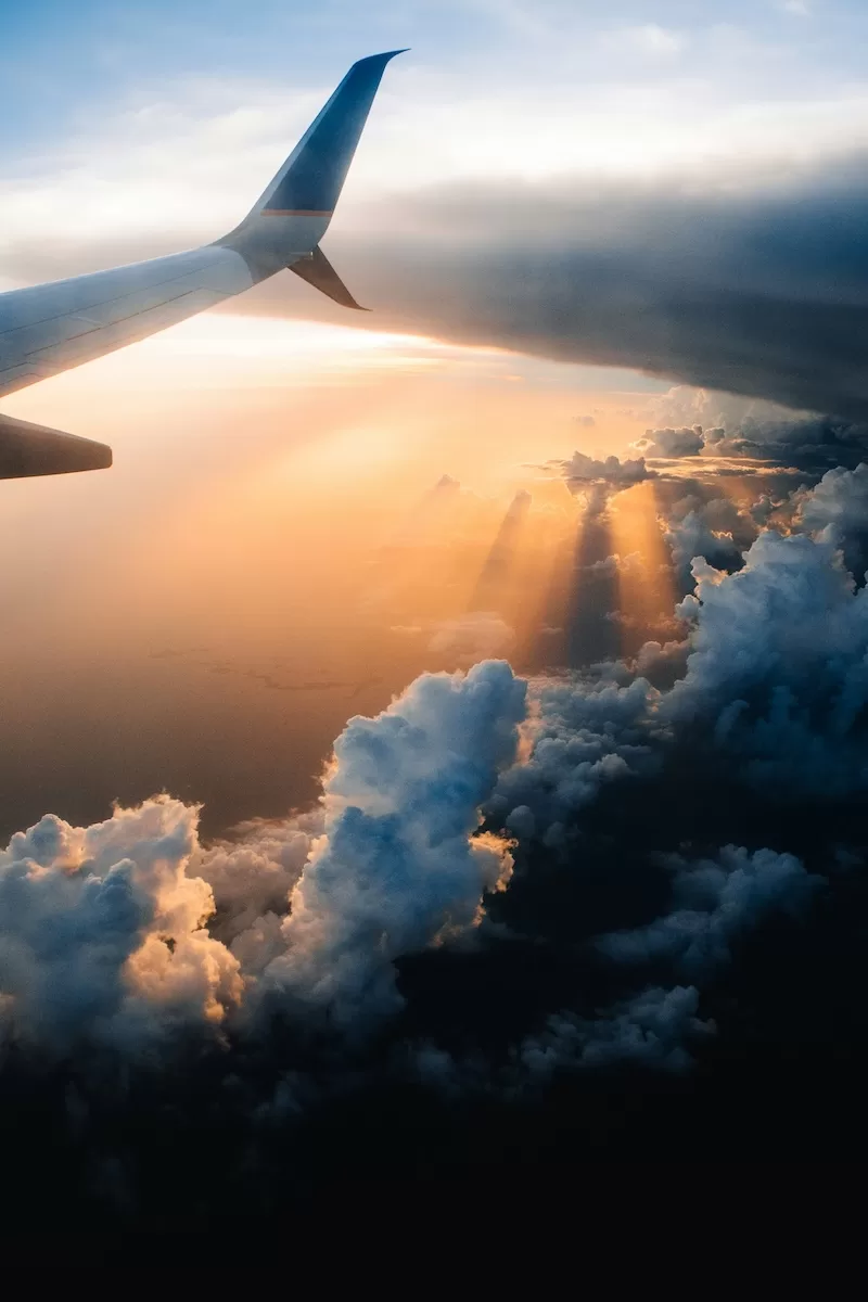 Airplane wing above clouds at sunset, representing global travel and second passport planning.