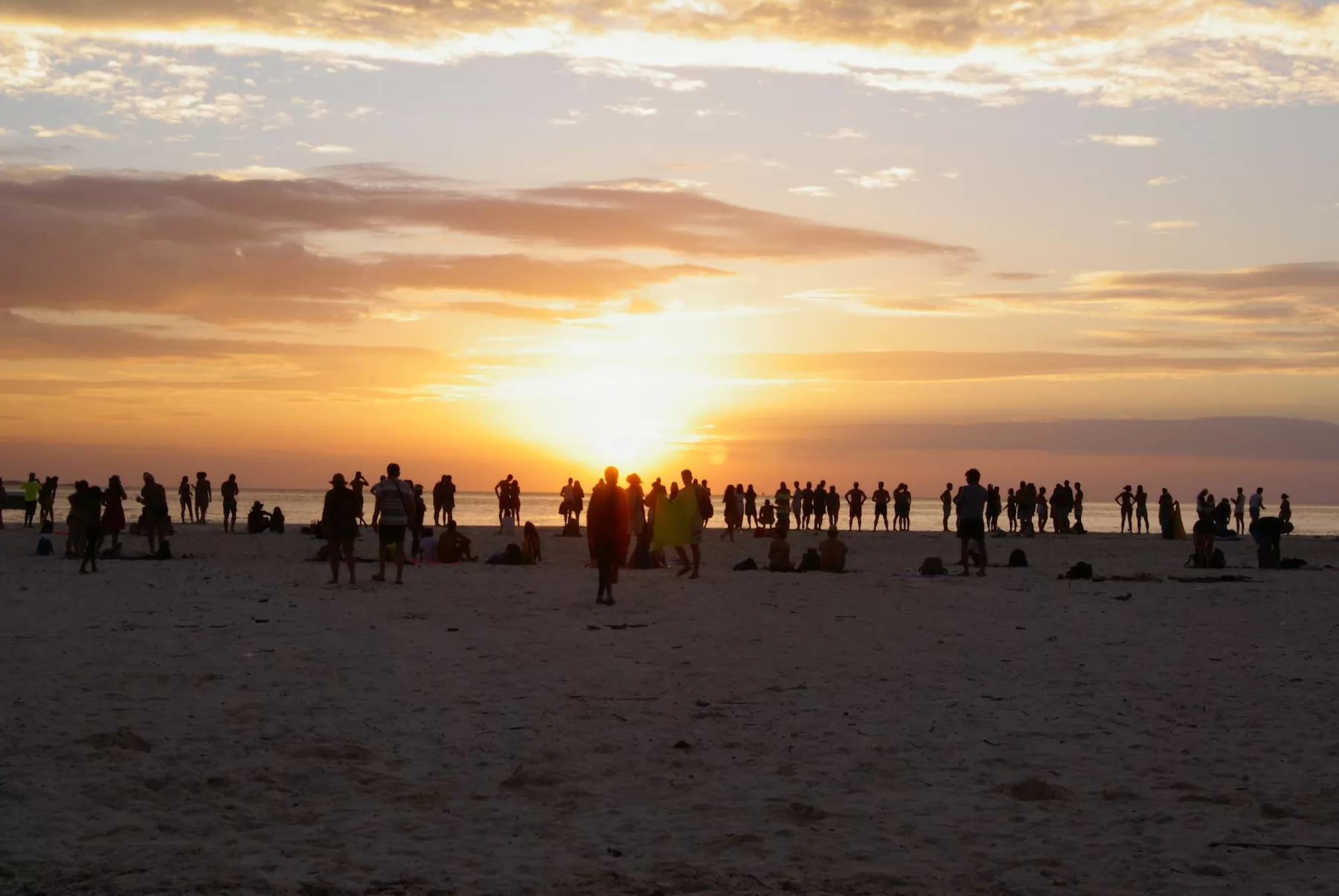 Silhouetted crowd watches the sun set over the ocean on a Zanzibar beach.
