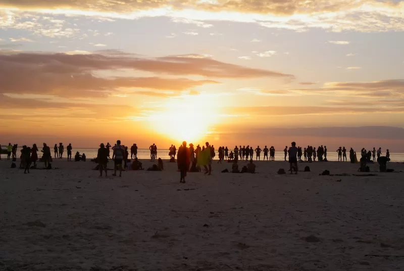 Silhouetted crowd watches the sun set over the ocean on a Zanzibar beach.