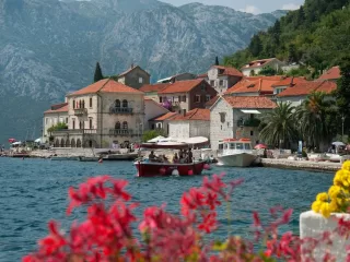 Historic waterfront village in Montenegro with red-roofed stone buildings and mountains behind the Bay of Kotor
