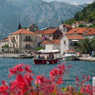 Historic waterfront village in Montenegro with red-roofed stone buildings and mountains behind the Bay of Kotor