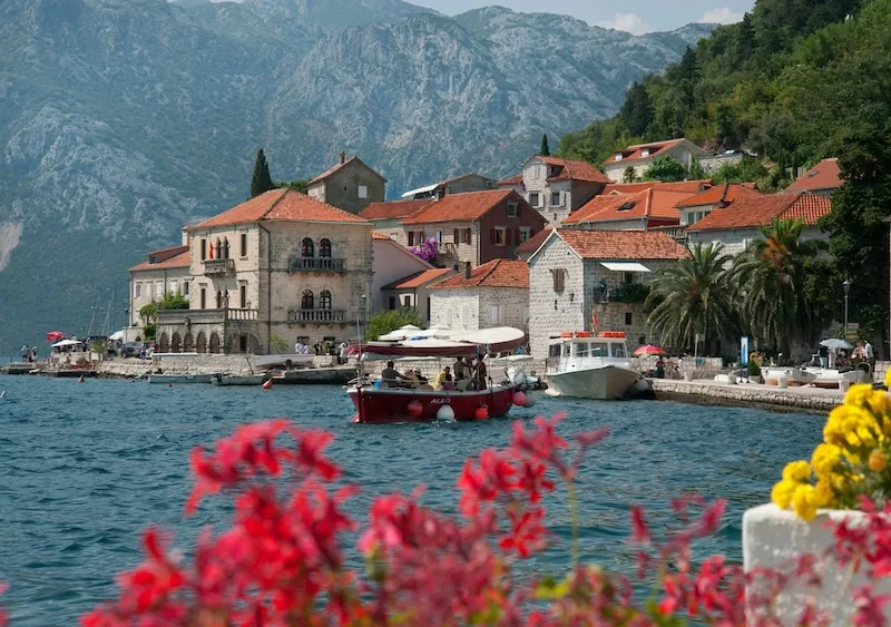 Historic waterfront village in Montenegro with red-roofed stone buildings and mountains behind the Bay of Kotor
