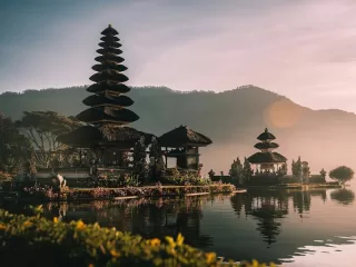 Balinese temple beside a lake at sunrise with mountains in the background