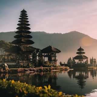 Balinese temple beside a lake at sunrise with mountains in the background