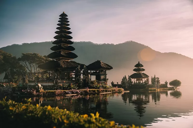 Balinese temple beside a lake at sunrise with mountains in the background