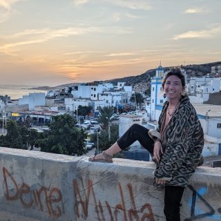 Woman sitting on a wall overlooking a coastal Moroccan town at sunset