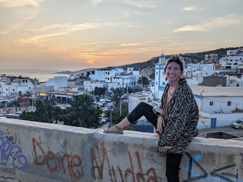Woman sitting on a wall overlooking a coastal Moroccan town at sunset